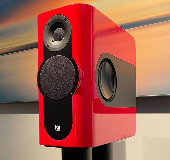 A rectangular speaker on a stand.  The speaker is bright red.  In the background there's a piece of art.