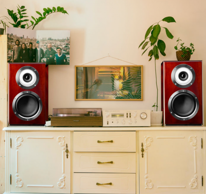 A pair of Cabasse Murano Loudspeakers in mahogany on a sideboard with a record player and amplifier in between.  There's a shelf with vinyl beside the sideboard.