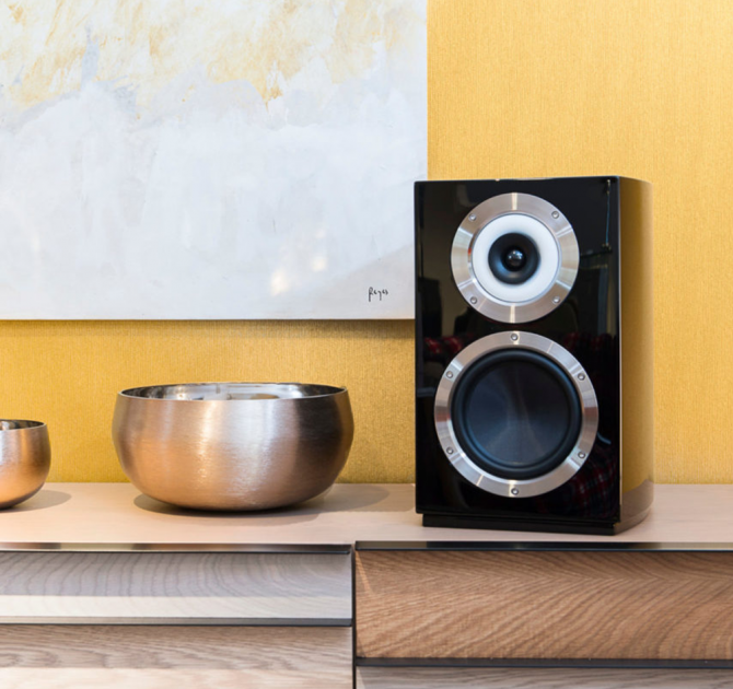 A Cabasse Murano Loudspeaker in black on a sideboard with a large bowl beside it.