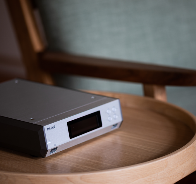 Melco N100 - HiRes Music Library.  Pictured on a wooden, circular table with a chair in the background.