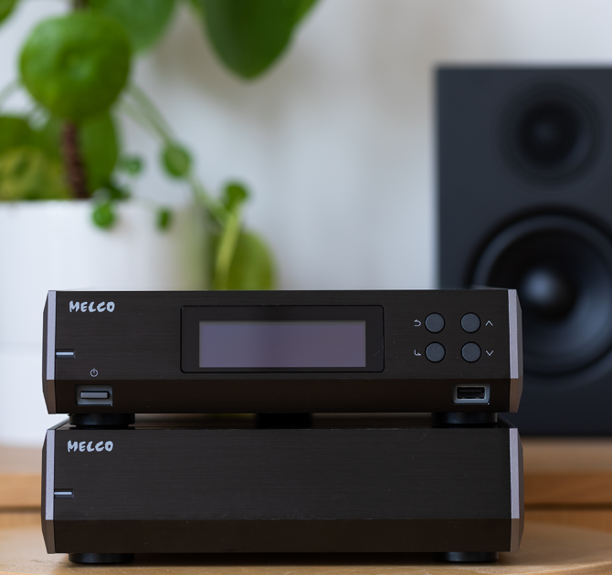 Melco N10/2 Digital Music Library in black on a wooden table with a speaker and plant in the background