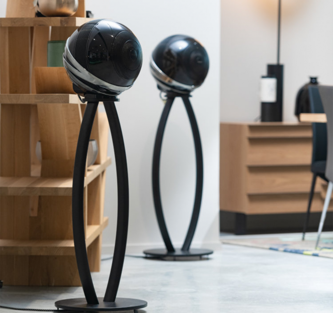 A pair of Cabasse Pearl Loudspeaker in black on stands in a living area with shelves and a chest of drawers