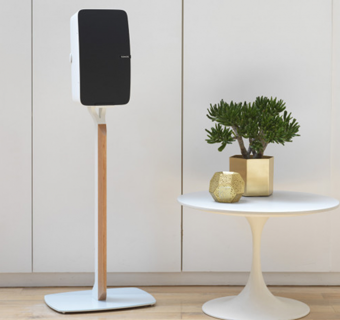 Flexson Premium Floor Stand Five x1 in white with a Sonos Play:5 vertically aligned next to a low white table with a gold, spherical vase and gold plant pot with a bushy green plant.