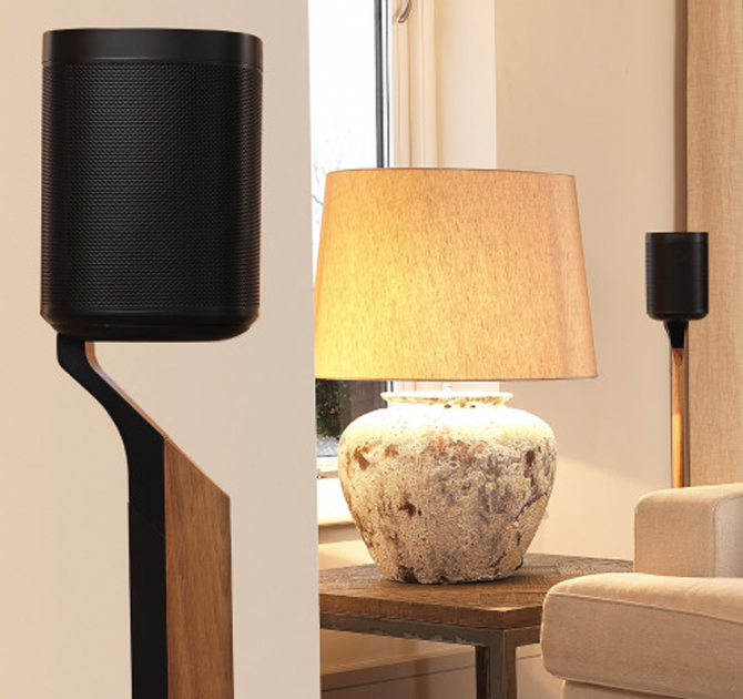 Flexson Premium Floor Stand One/Play1 Blk x1 - Black in a living room with a large table lamp and a second speaker on a Premium stand in the background.