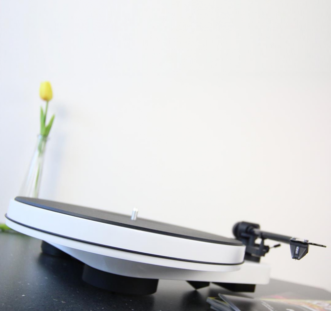 Project RPM 3 Carbon - Turntable in white photographed at an angle on a granite worksurface with a yellow tulip in a tall vase in the background. 