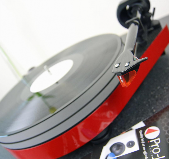 Project RPM 5 Carbon - Turntable in red pictured at an angle with a project catalogue to the side