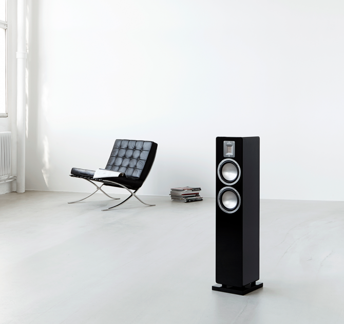 Audiovector QR3 in piano black in the foreground and a black chair in the background.