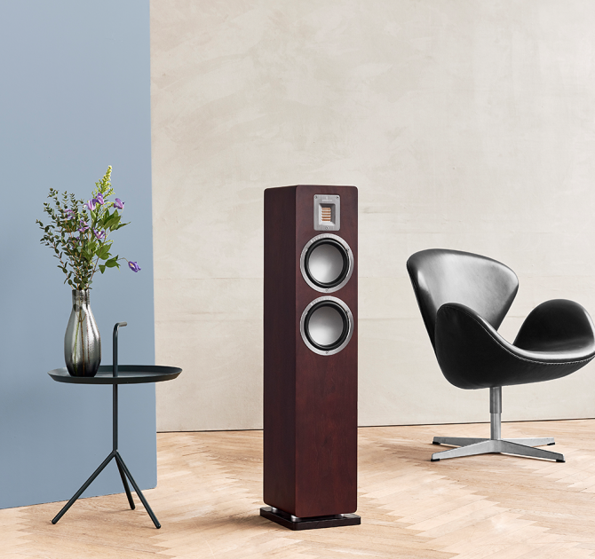 Audiovector QR3 in dark walnut with a chair beside it and a small table holding a vase of flowers the other side.