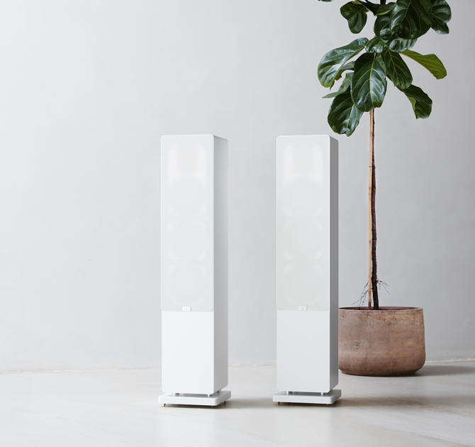 Audiovector QR5 pair of white speakers with grilles on next to a tall houseplant.