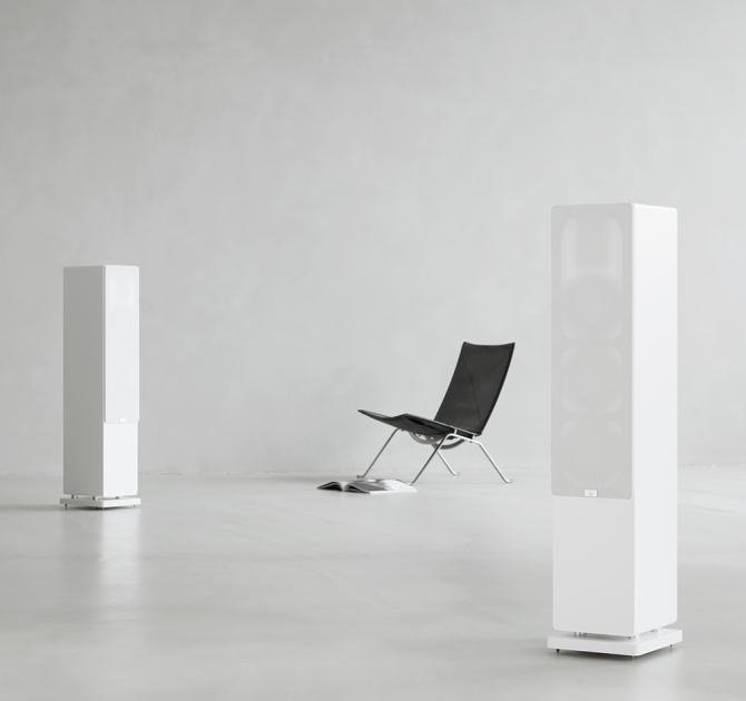 Audiovector QR5 pair in white with grilles on and a chair between them.