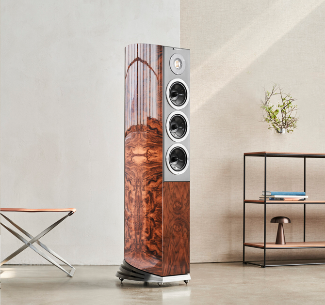 Audiovector R8 Arreté Loudspeaker in Italian Walnut Burl beside a table and shelves on the right