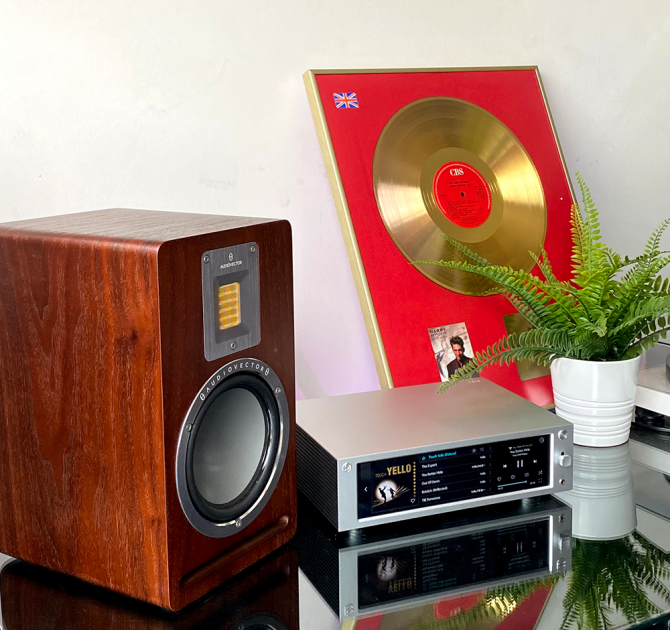 Rose RS-201E Streamer, DAC and amplifier showing 'Yello' playing, and Audiovector speaker beside it and a mug.