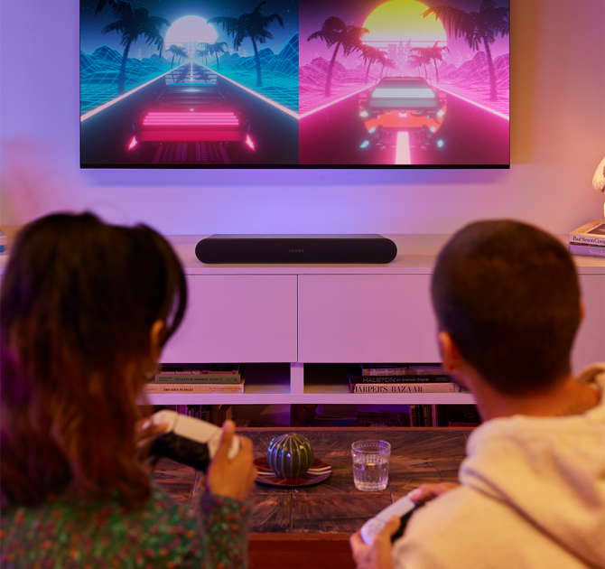 Sonos Ray Smart Soundbar in black with a tv mounted on the wall and a couple of people gaming in the foreground