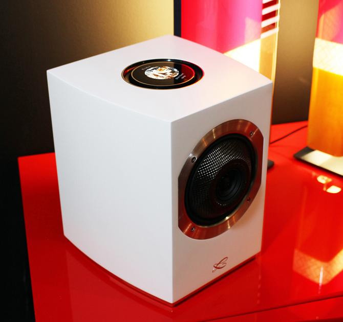 A Cabasse Rialto Loudspeaker in white on a red table with a coloured light in the background