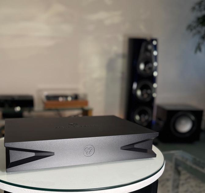 Kudos Sigao drive in black on a circular white table with a Linn 360 speaker in the background along with a turntable and a DSM