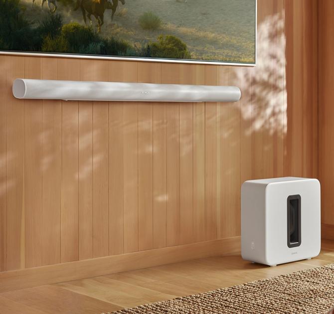 SONOS Arc Ultra Smart Soundbar in white underneath a tv screen with a Sonos sub on the floor