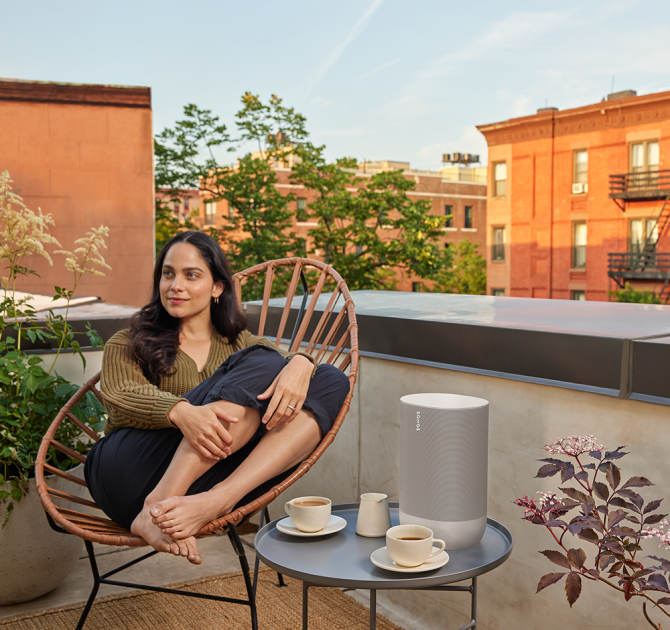 SONOS Move on a small table beside a lady curled in a chair on a rooftop in a city