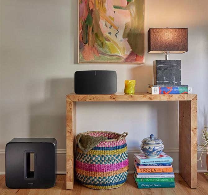 Sonos Sub Gen 4 in black on the floor beside a side table with a speaker and lamp