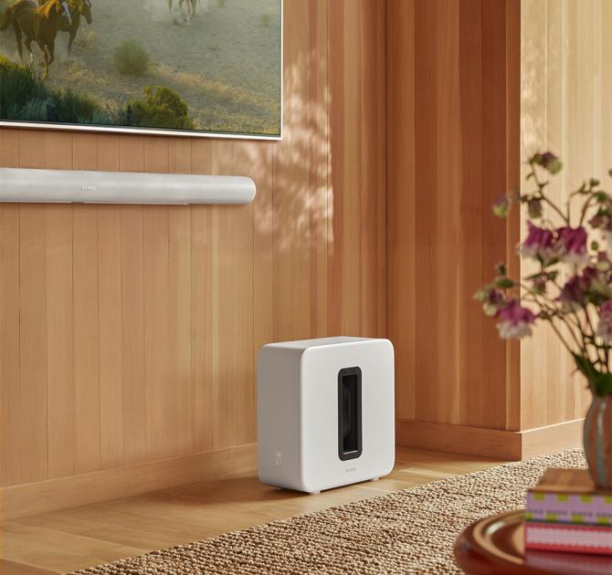 Sonos Sub Gen 4 in white on the floor with a tv wall mounted and a Sonos Arc underneath the TV.