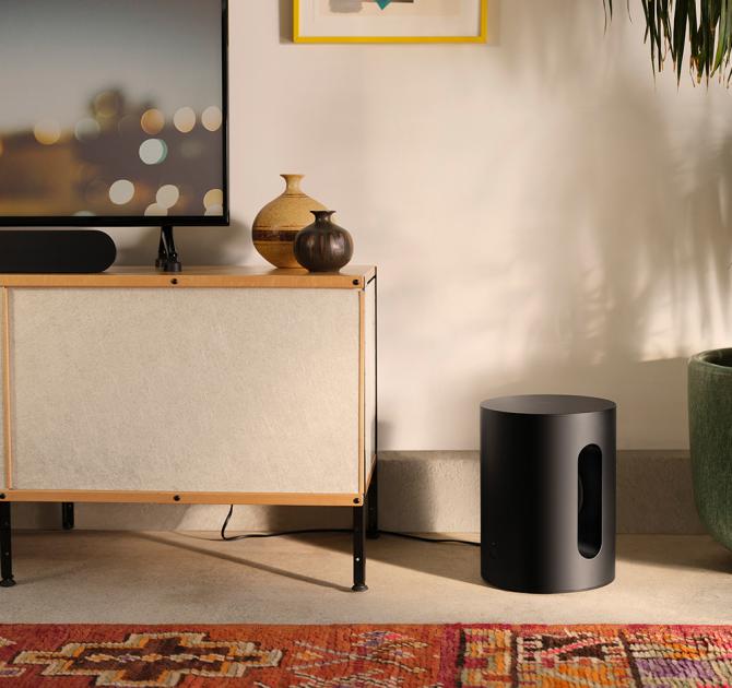 SONOS Sub Mini in black on the florr beside a sideboard in a living room