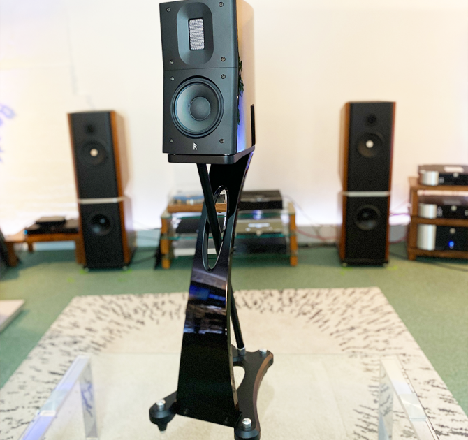 Raidho Acoustics TD1.2 Speaker in black on a glass table in the ripcaster showroom with other HiFi equipment in the background including Kudos 808 speakers and a Linn LP12.