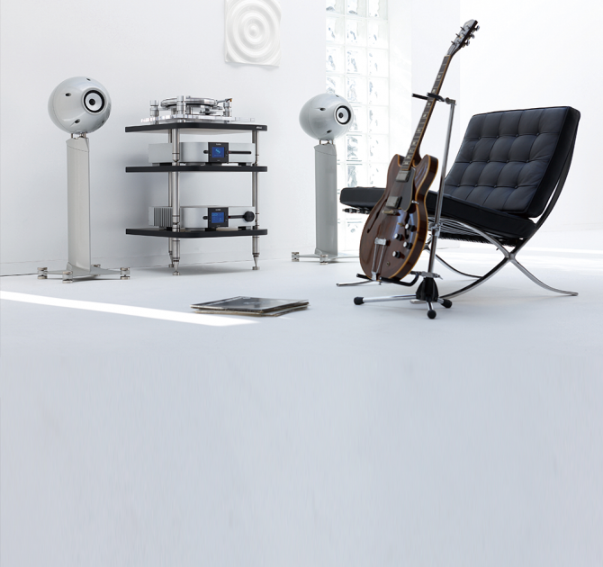 Eclipse TD712zMK2 Speaker on Stand (Single) in silver with a hifi system on shelves, a chair and a guitar.