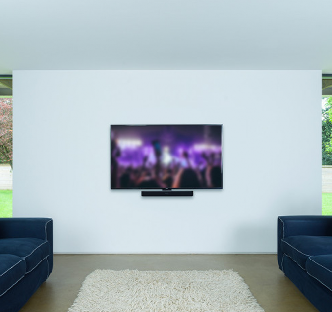 Flexson Adjustable Wall Mount Beam x1 fixed to a wall with a Sonos Beam in place and a TV above.  Fixed on a light coloured wall with a navy sofa either side  The sofas are facing each other.