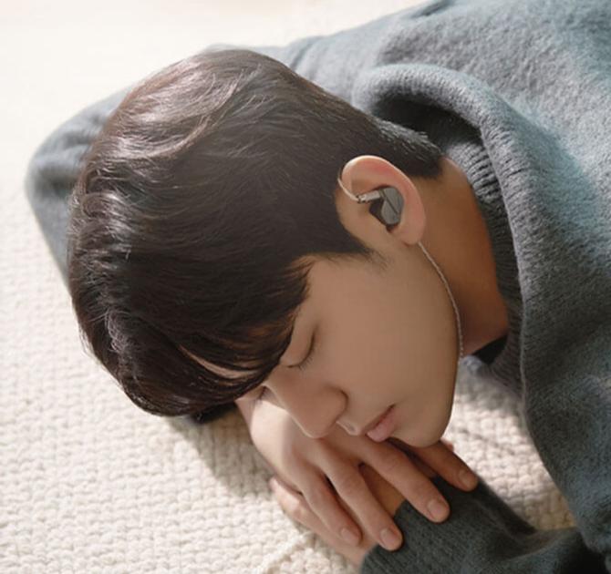 Astell & Kern Zero 2 Earphones in a young man's ear.  He's wearing a grey top