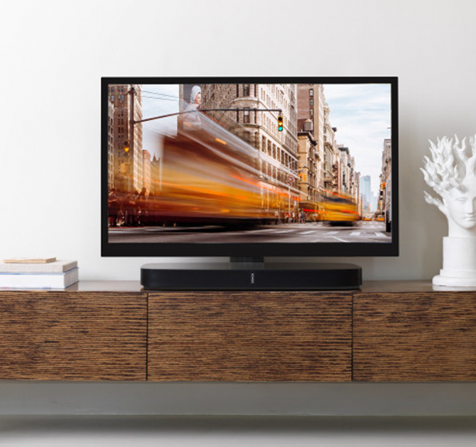 Flexson Adjustable TV Stand Playbase x1 in black with a Playbase and TV on a wooden cabinet.