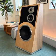 Audiovector Trapeze Ri in nordic oak.  Photo taken in the ripcaster showroom with a tall plant in the background and vinyl in wooden boxes