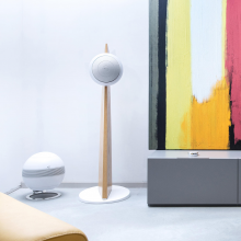 Cabasse Baltic 5 Sub System (on stand).  The sub is white.  The Baltic 5 is white on a wooden stand.  It's beside a low sideboard with abstract art on the wall.