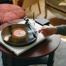 Project E1 Turntable on a small table with a person's arm reaching over and putting the needle on the record