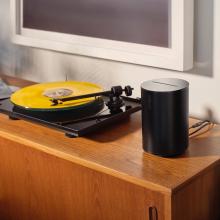 SONOS Era 100 Loudspeaker in black beside a black turntable playing a yellow record