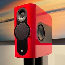 A red rectangular speaker on a black stand.  In the background there is a large piece of art.