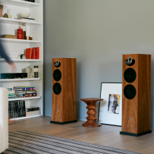 a pair Linn Majik 140 Loud Speakers with a table between them and a set of shelves to the side.