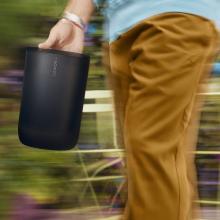 A man in light brown trousers carrying the SONOS Move 2 Loudspeaker in black