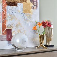 Cabasse Pearl Loudspeaker in white on a sideboard with flowers and an abstract picture behind.