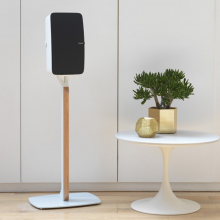 Flexson Premium Floor Stand Five x1 in white with a Sonos Play:5 vertically aligned next to a low white table with a gold, spherical vase and gold plant pot with a bushy green plant.