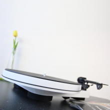 Project RPM 3 Carbon - Turntable in white photographed at an angle on a granite worksurface with a yellow tulip in a tall vase in the background. 