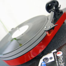 Project RPM 5 Carbon - Turntable in red pictured at an angle with a project catalogue to the side