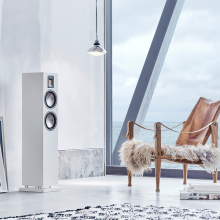 Audiovector QR3 in white silk beside a window with a seaview and with a chair in front of it.