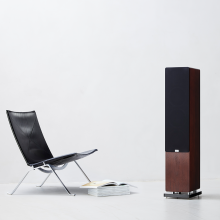 Audiovector QR5 - a single dark walnut speaker with grille on and a chair beside it.