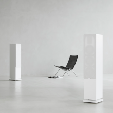 Audiovector QR5 pair in white with grilles on and a chair between them.
