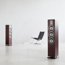 Audiovector QR5 pair in dark walnut with a chair between them.