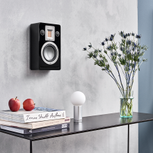 Audiovector QR Wall in piano black on a wall above a table with books and a vase of flowers on.