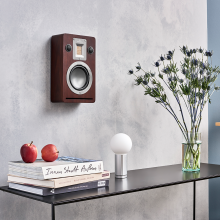 Audiovector QR Wall in dark walnut on a wall above a table with books, a lamp and flowers on