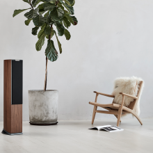 Audiovector R3 Arreté in Italian Walnut, grille on with a large houseplant and a chair