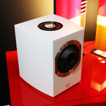 A Cabasse Rialto Loudspeaker in white on a red table with a coloured light in the background