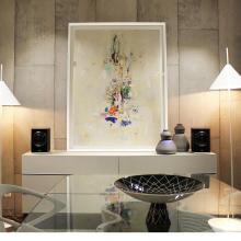 A pair of Cabasse Rialto Loudspeakers in black on top of a unit either side of a piece of abstract art with some vases.