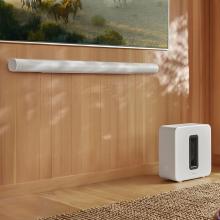 SONOS Arc Ultra Smart Soundbar in white underneath a tv screen with a Sonos sub on the floor